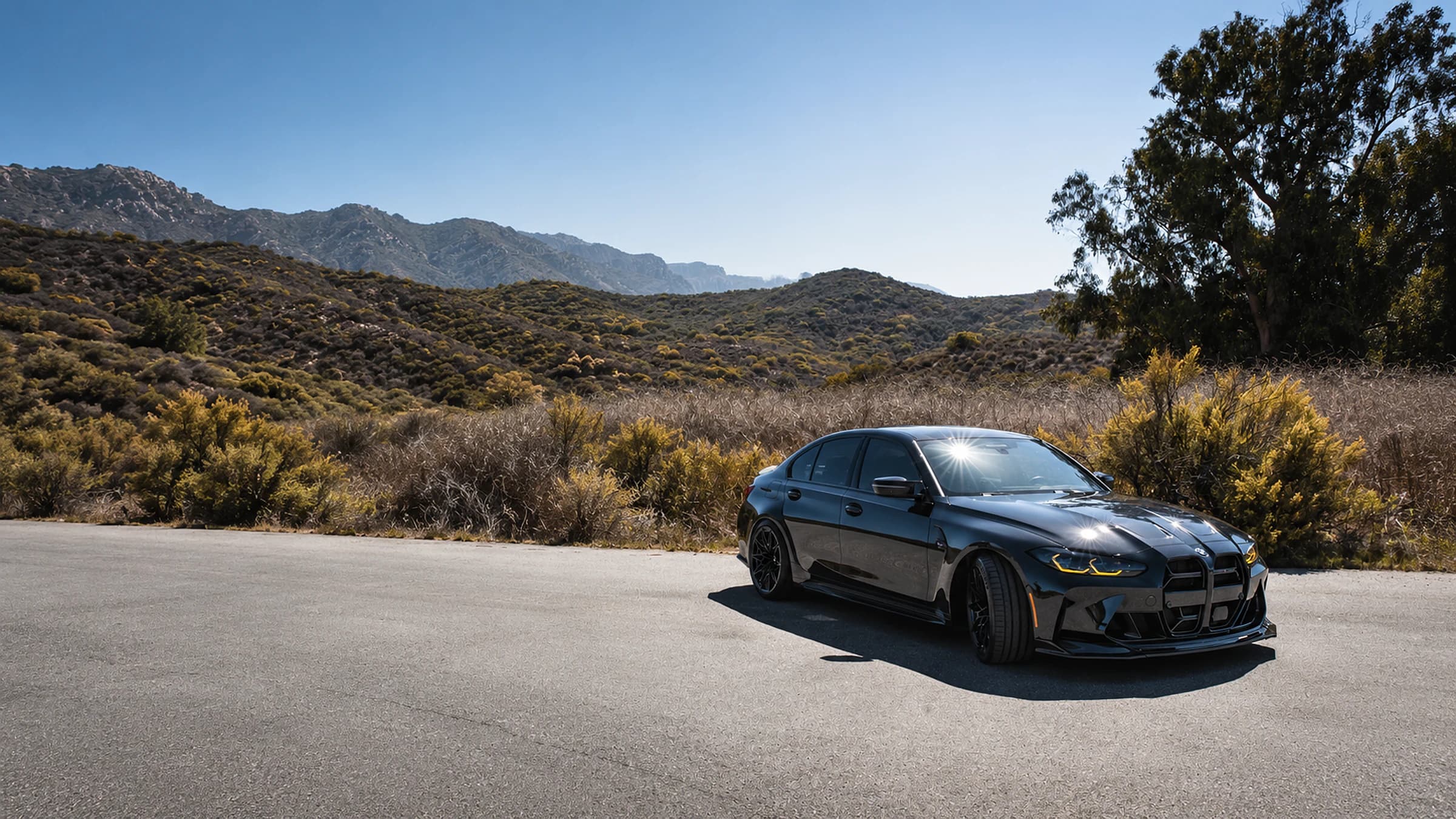 Black BMW performance sedan photographed in full on a Southern California mountain road